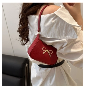 Detail of red lychee leather underarm bag with a golden metal bow and shoulder strap
