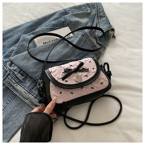 Détail du sac bandoulière rose en tissu gaufré avec nœuds noirs et pendentif cœur