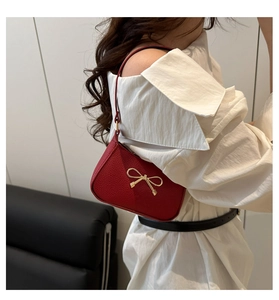 Détail du sac à bandoulière rouge texture lychee avec un nœud doré et sangle fine
