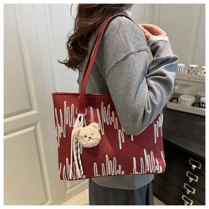 Detail of dark red tote bag with wave embroidery and cream plush bear charm