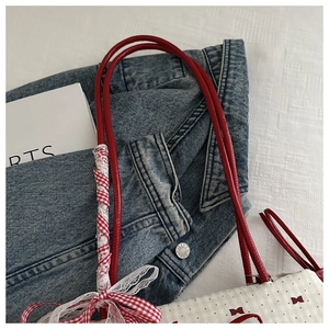 Détail du sac bandoulière en toile blanche avec nœud rouge et bandoulière cylindrique