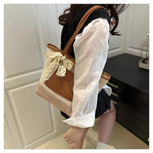 Detail of cream straw bucket bag with brown leather trim and lace bow on a model