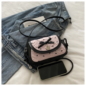 Détail du sac plissé rose avec des nœuds noirs et un pendentif en forme de cœur argenté