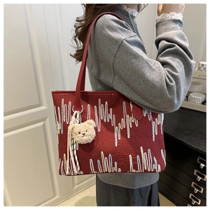 Detailed side view of red tote bag with wave pattern embroidery and plush bear charm