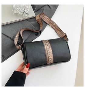 Detail of black pebbled leather cylinder bag featuring a retro bohemian woven strap