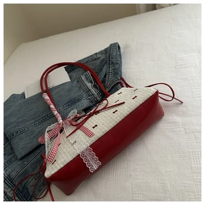Détail du sac à bandoulière à nœud rouge et blanc avec dentelle et ruban sur lit doux