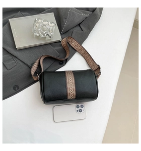 Top view of black pebbled leather cylinder bag with geometric strap and phone for scale