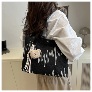 Detail of black embroidered tote bag with plush bear charm and textured fabric finish