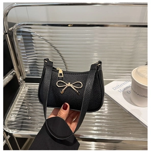 Détail de la texture cuir noir et du fermoir nœud en métal doré sur le sac à main chic