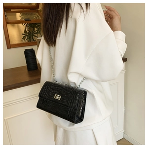 Close-up of black crocodile embossed texture with silver chain and metal clasp detail