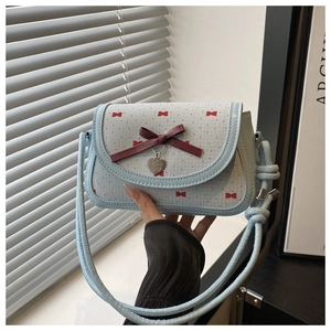Détail du sac bandoulière bleu clair avec nœud papillon rouge et breloque en cœur