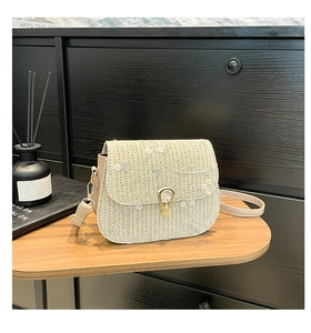 Détail de la broderie florale et du fermoir doré sur un sac à bandoulière en paille