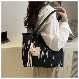 Detail of black tote bag with wave embroidery, plush bear charm and woven tassels