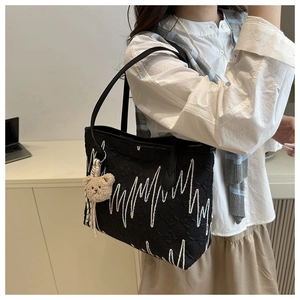 Detail of black tote bag with wavy embroidery, floral texture and plush bear charm