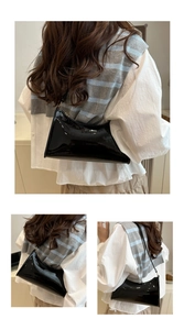Close-up of black patent leather baguette bag featuring glossy finish and minimalist design