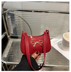 Détail d'un sac à main rouge à motif litchi avec boucle nœud dorée et fermeture éclair