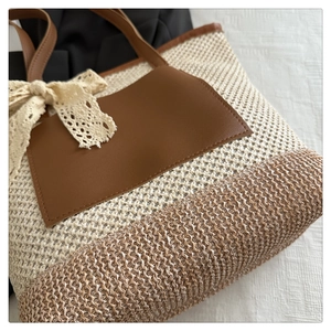 Close-up of woven straw tote bag featuring a leather pocket and beige lace bow detail
