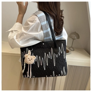 Detail of black tote bag with wave embroidery and brown plush bear charm on the strap