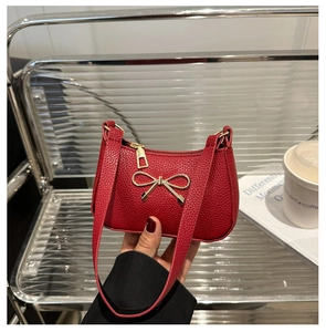 Gros plan d'un sac à main rouge en cuir grainé avec un nœud doré métallique