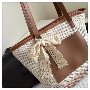 Close-up of woven straw tote bag featuring faux leather patches and lace bow detail