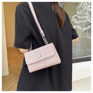Close-up of light pink croc-effect crossbody bag with silver chain strap on a model