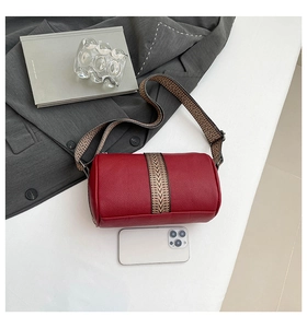 Macro shot of red pebble leather cylindrical bag with ethnic patterned strap and phone for scale