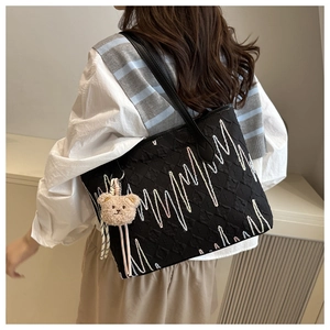 Detail of black tote bag featuring textured fabric with wave embroidery and plush bear charm