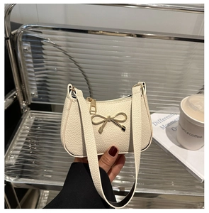 Détail du sac crème à texture grainée avec un nœud doré et une bandoulière fine en cuir