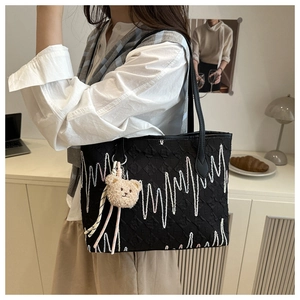 Detail of black tote bag with white wave embroidery and plush bear charm on shoulder