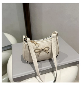 Détail du sac en cuir grainé blanc crème avec un nœud décoratif doré sur le devant