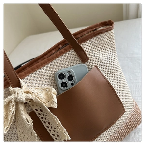 Detail of woven tote bag with brown leather pocket, lace bow, and mobile phone storage