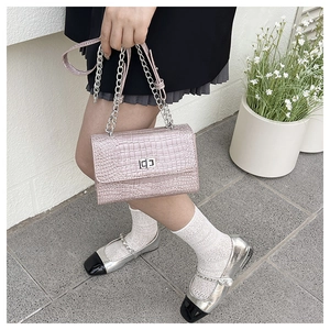 Detail of pink crocodile embossed handbag featuring a silver chain strap and metal lock