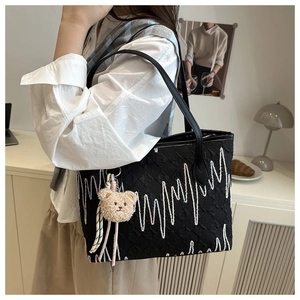 Detailed view of black tote bag with wavy embroidery and cute bear plush charm
