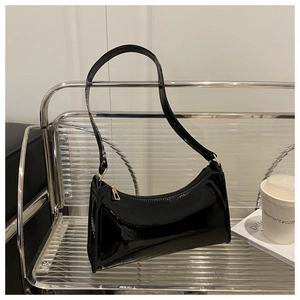 Detail of glossy black patent leather shoulder bag with gold hardware zipper and sleek texture