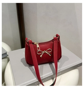 Détail d'un sac à main rouge en cuir grainé avec nœud doré et fermeture éclair chic