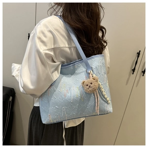 Detail of light blue tote bag featuring embossed letters and colorful embroidery