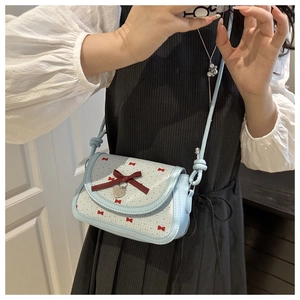 Détail d'un sac bandoulière bleu avec nœuds rouges et pendentif coeur en métal
