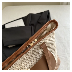 Detail of woven straw tote bag with brown leather trim and gold zipper closure