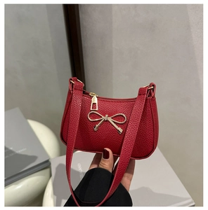 Détail d'un sac rouge en cuir litchi avec une décoration élégante de nœud doré en métal