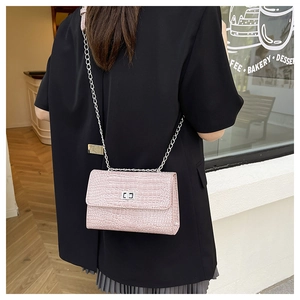 Detail of pink croc-embossed flap bag with silver twist lock and metal chain strap