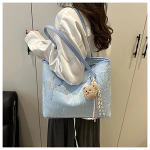 Detail shot of light blue tote bag with geometric texture and plush bear charm on model