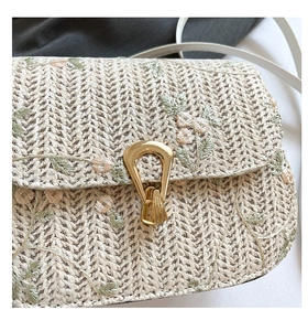 Detail of floral embroidery and gold metal clasp on woven cream straw shoulder bag