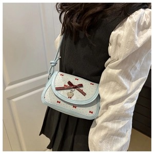 Détail du sac à bandoulière bleu clair avec nœuds rouges et pendentif en métal