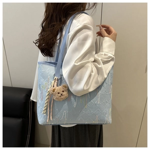 Detail of light blue tote bag featuring embossed E-pattern and brown plush bear charm