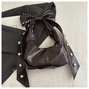 Detail of dark brown glossy patent leather bag with oversized bow and silver rivets