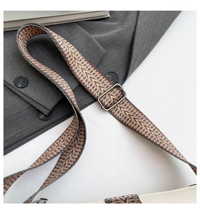 Detail of woven geometric shoulder strap with metal buckle on white leather bag