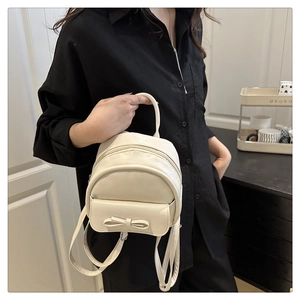 Detailed view of white mini backpack with bow knot held by model in black outfit
