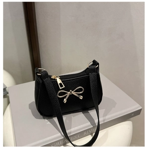 Détail d'un sac en cuir noir à motif litchi avec une boucle dorée en forme de nœud chic