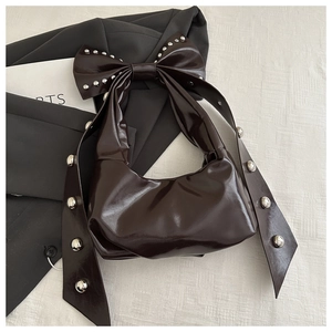 Detailed view of dark brown glossy handbag with large bow and silver rivet accents