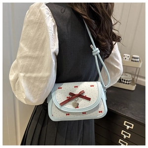 Détail d'un sac bandoulière bleu clair avec nœud rouge et pendentif cœur sur modèle